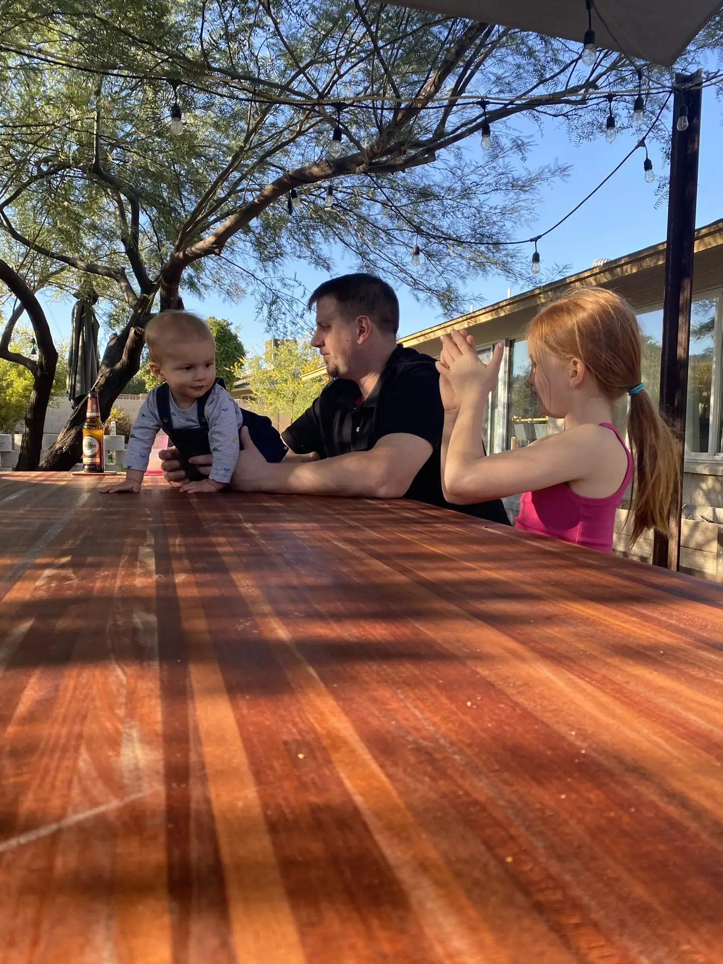 A family seated at a solid-wood outdoor table under string lights