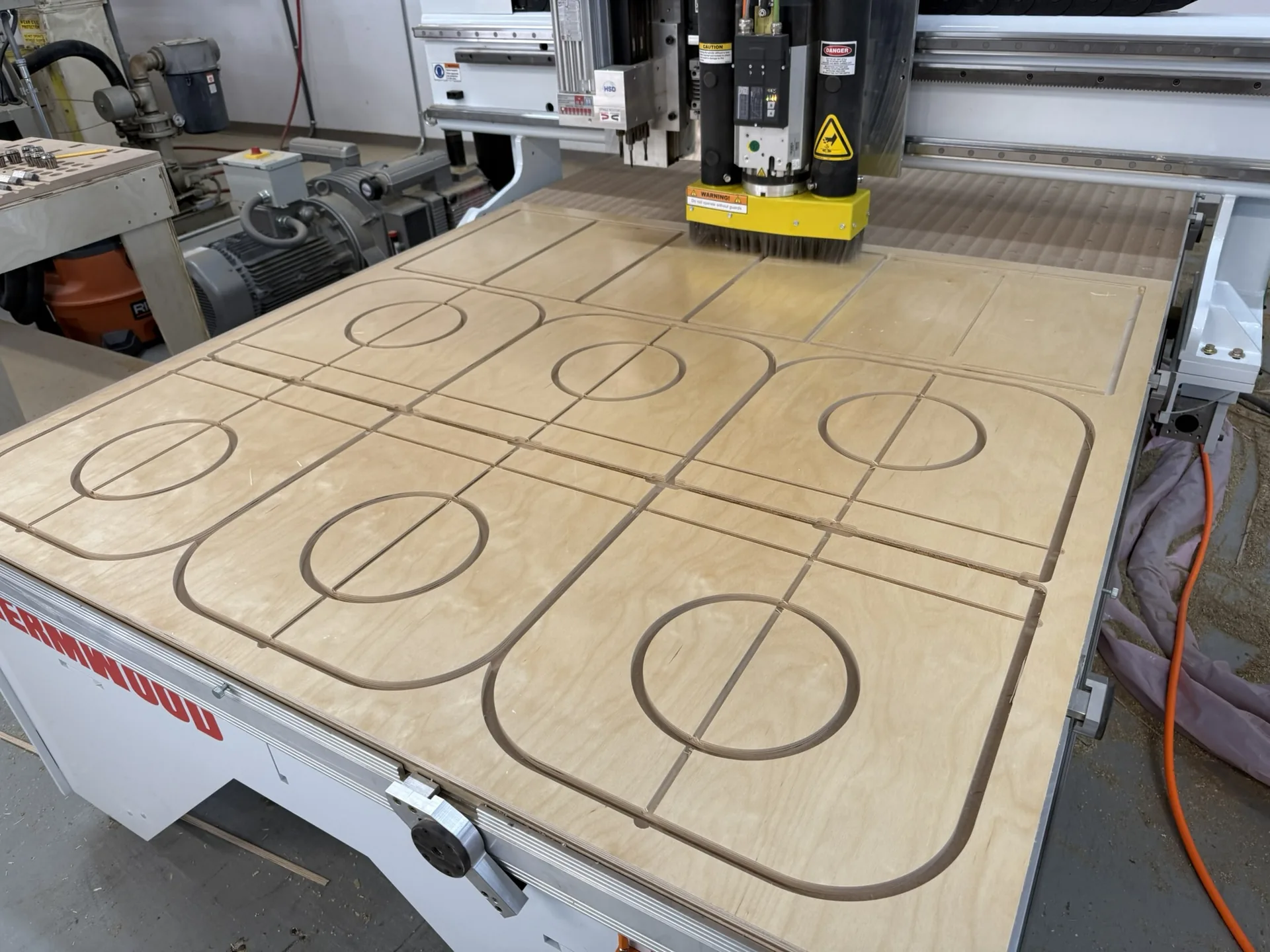 Cabinet parts nested and cut into a plywood sheet on the CNC table, cut paths still visible