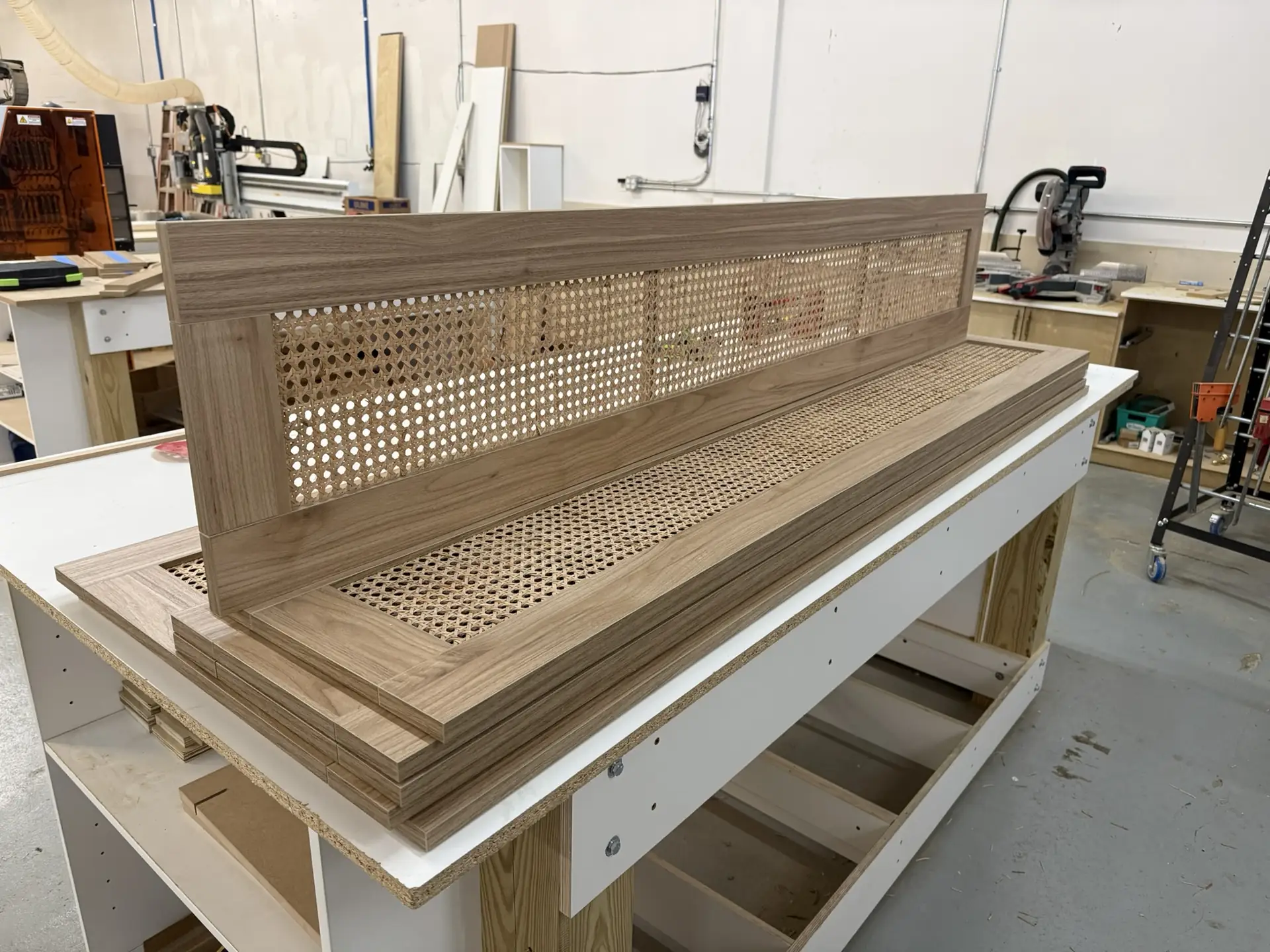 A caned rattan panel set into a white oak frame, resting on the assembly bench