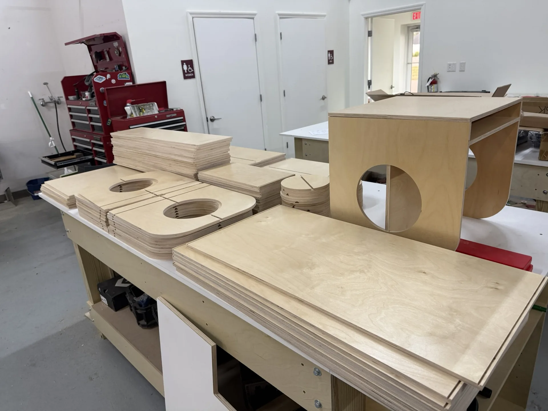 Birch plywood parts with routed circular cutouts, stacked on the bench after machining