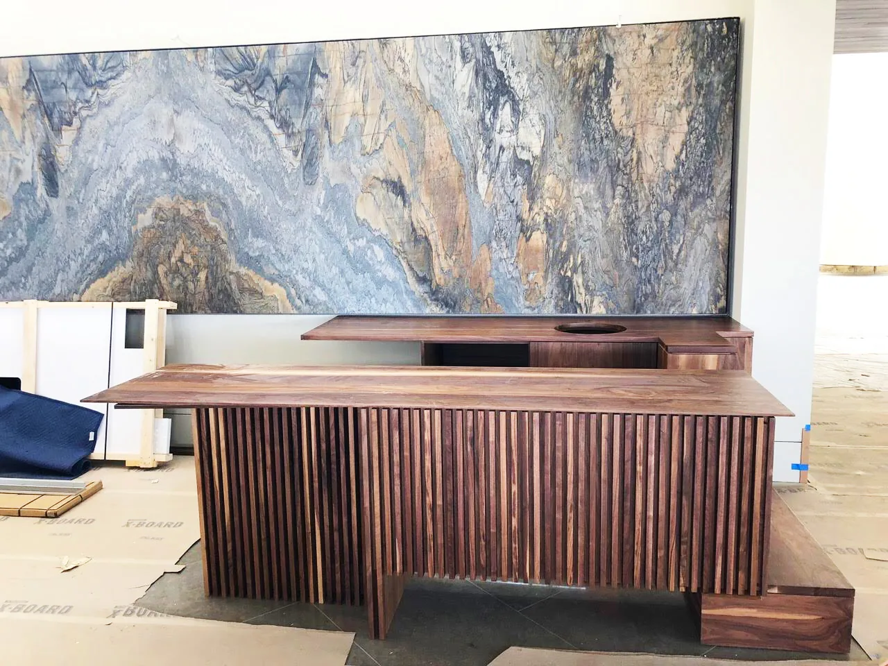 A walnut reception desk with a fluted front, set against a full-height stone slab wall