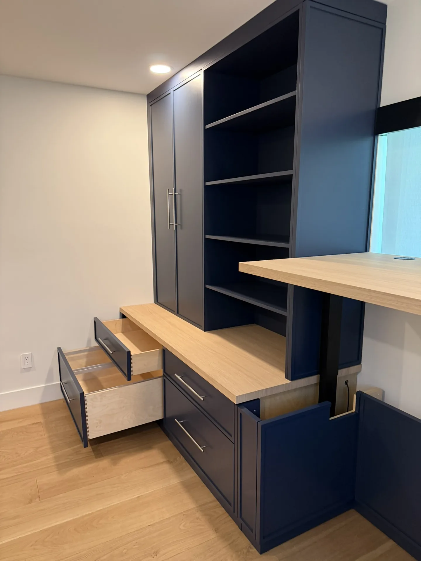 A navy lacquered built-in with white oak shelving and drawers, drawers pulled open