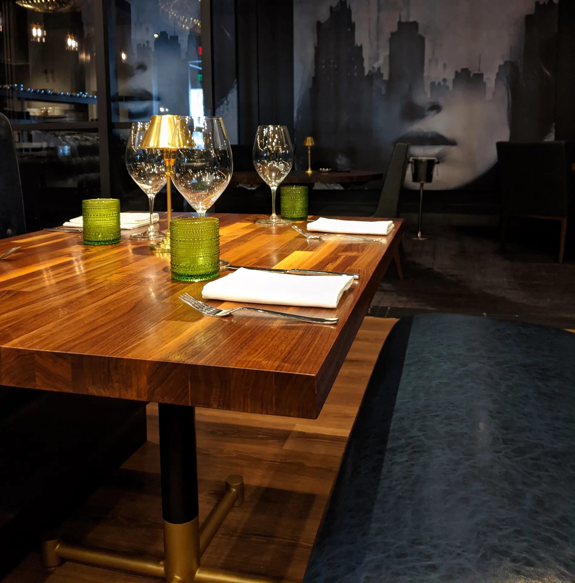 A walnut dining table set with glassware and linen in a dark restaurant interior