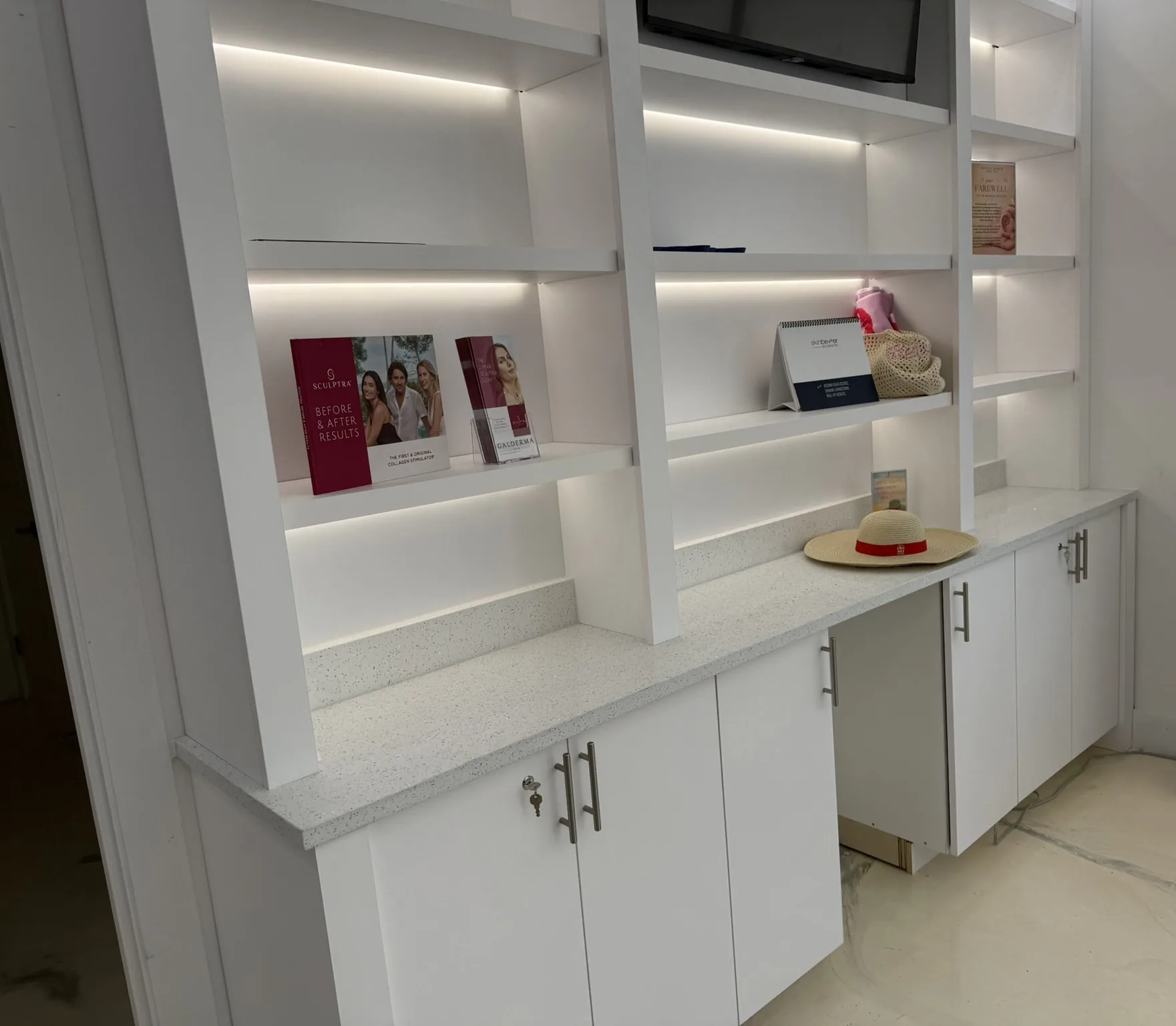 A white built-in with lit display shelving above a quartz counter and base cabinets