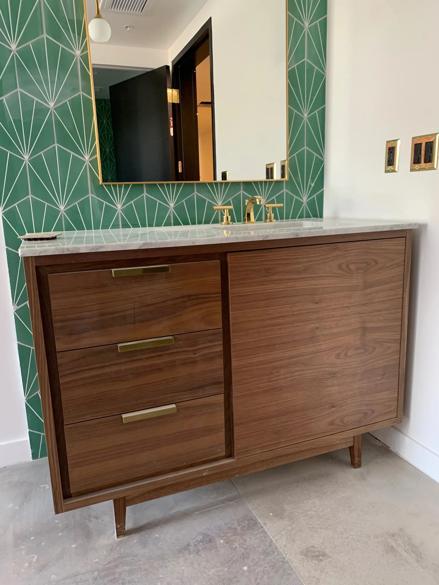 A walnut vanity with brass pulls against a green geometric tile wall