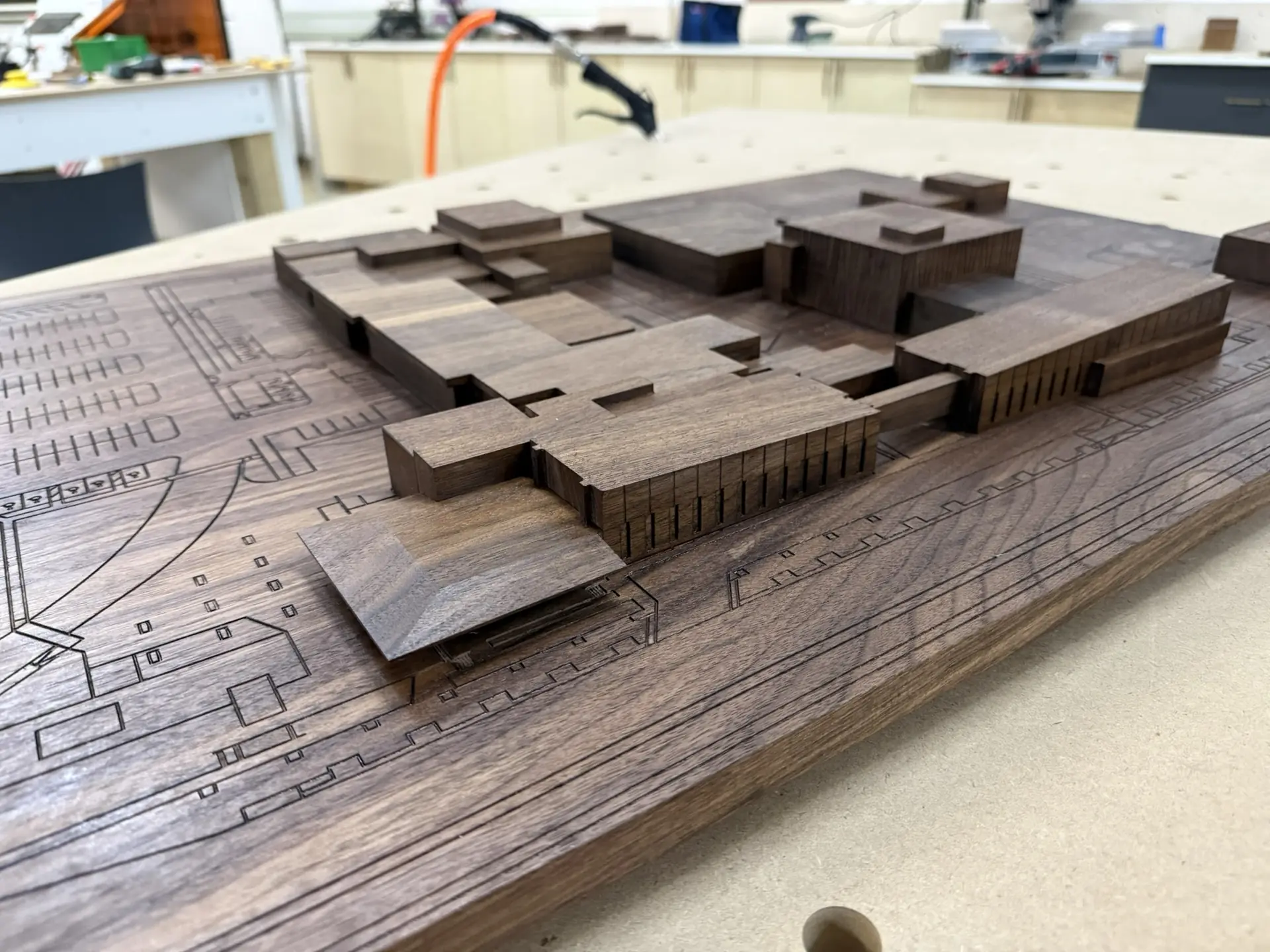 A walnut architectural model of a campus, photographed on the shop bench