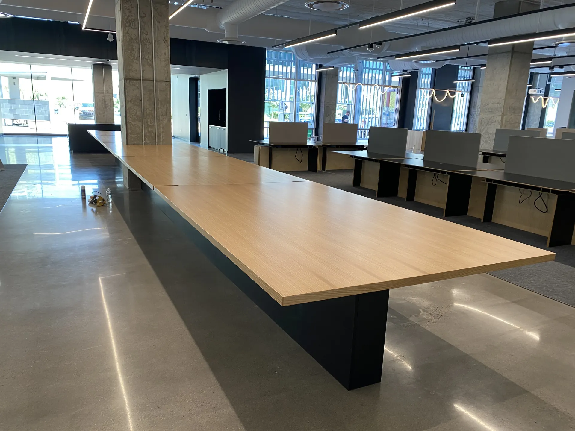 A long white oak conference table on a blackened blade base in an open office