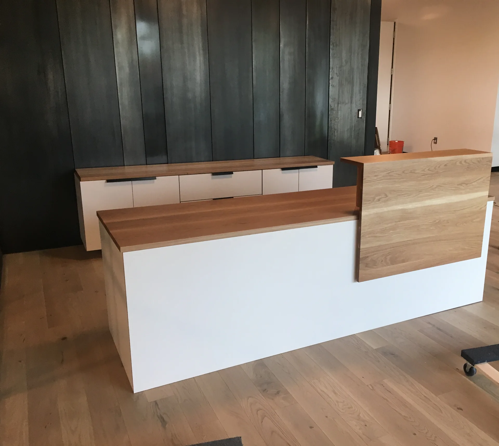 A white and white oak reception desk against a dark vertical slat wall