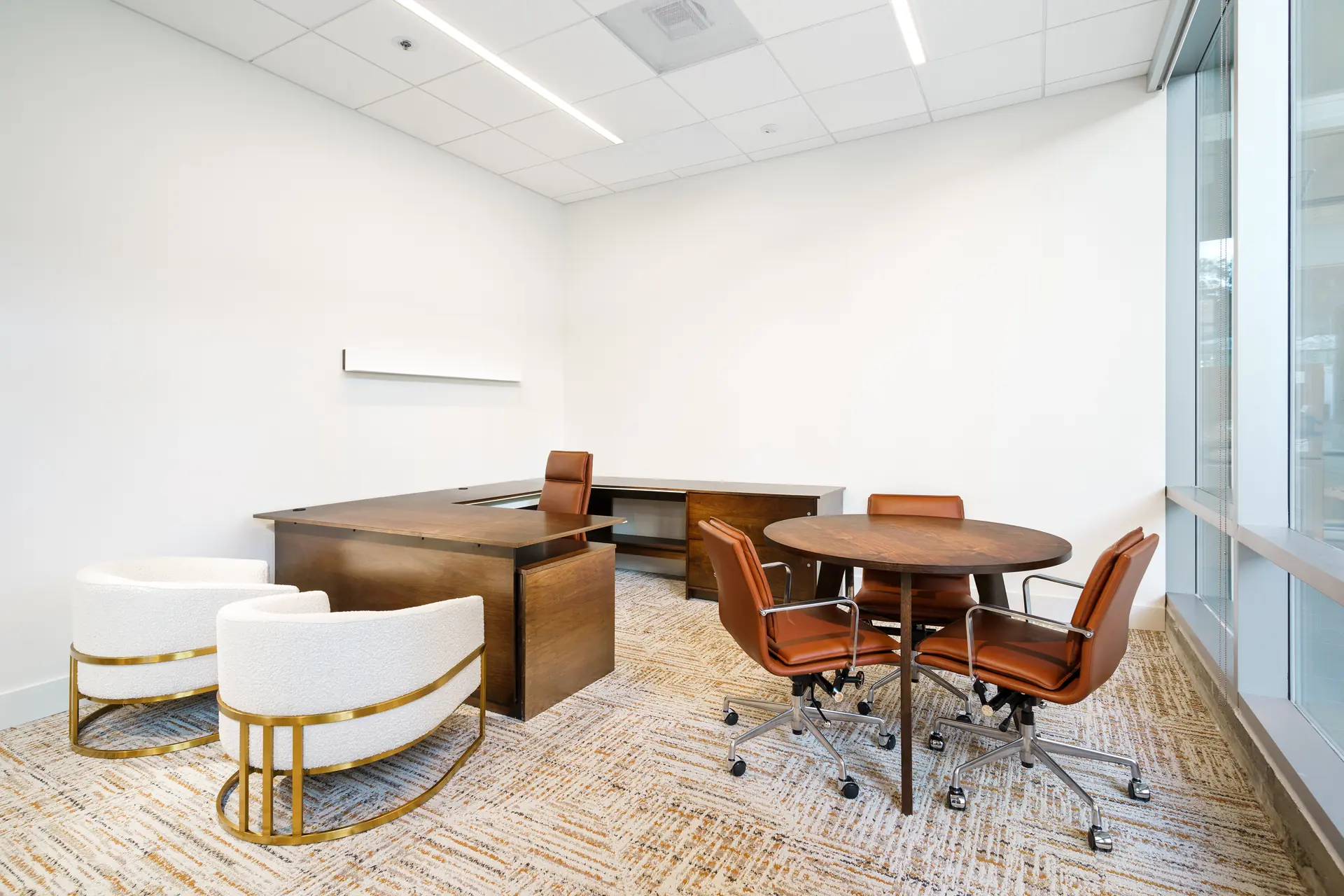A private office with a walnut desk, round meeting table and lounge chairs