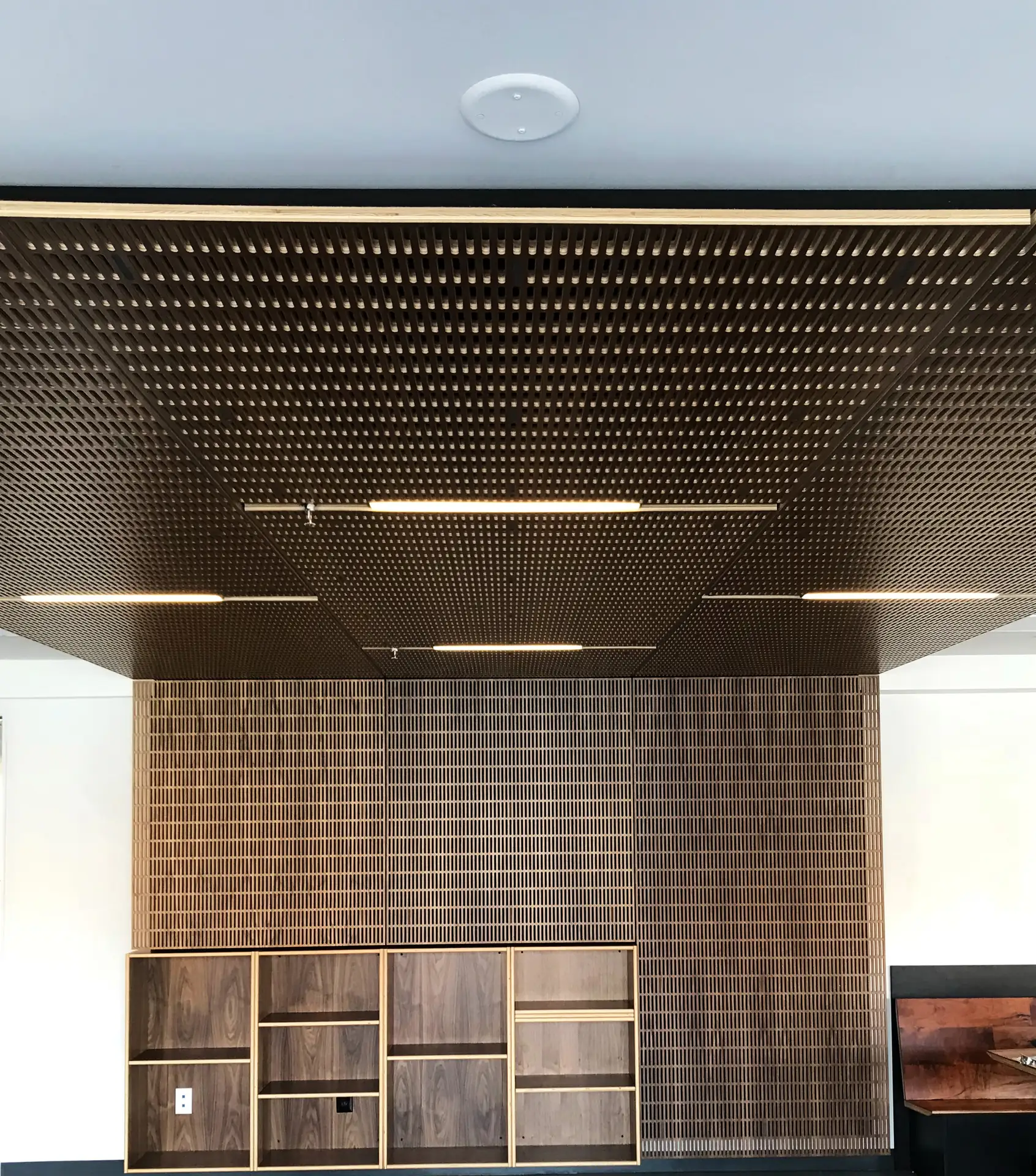 A perforated walnut feature wall with integrated lighting and open shelving below