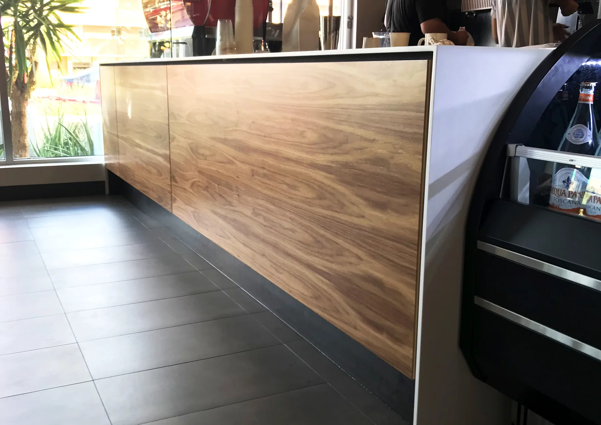 A coffee shop service counter faced in figured wood with a stainless top edge