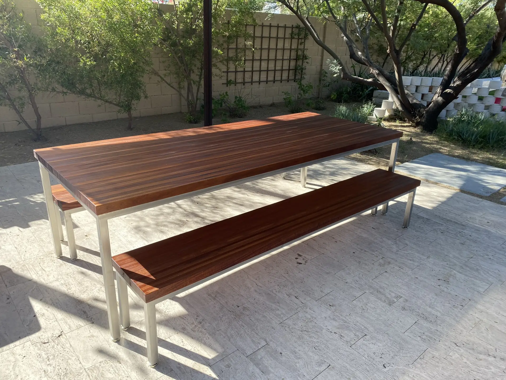 A solid hardwood outdoor table and matching benches on steel bases, in a courtyard