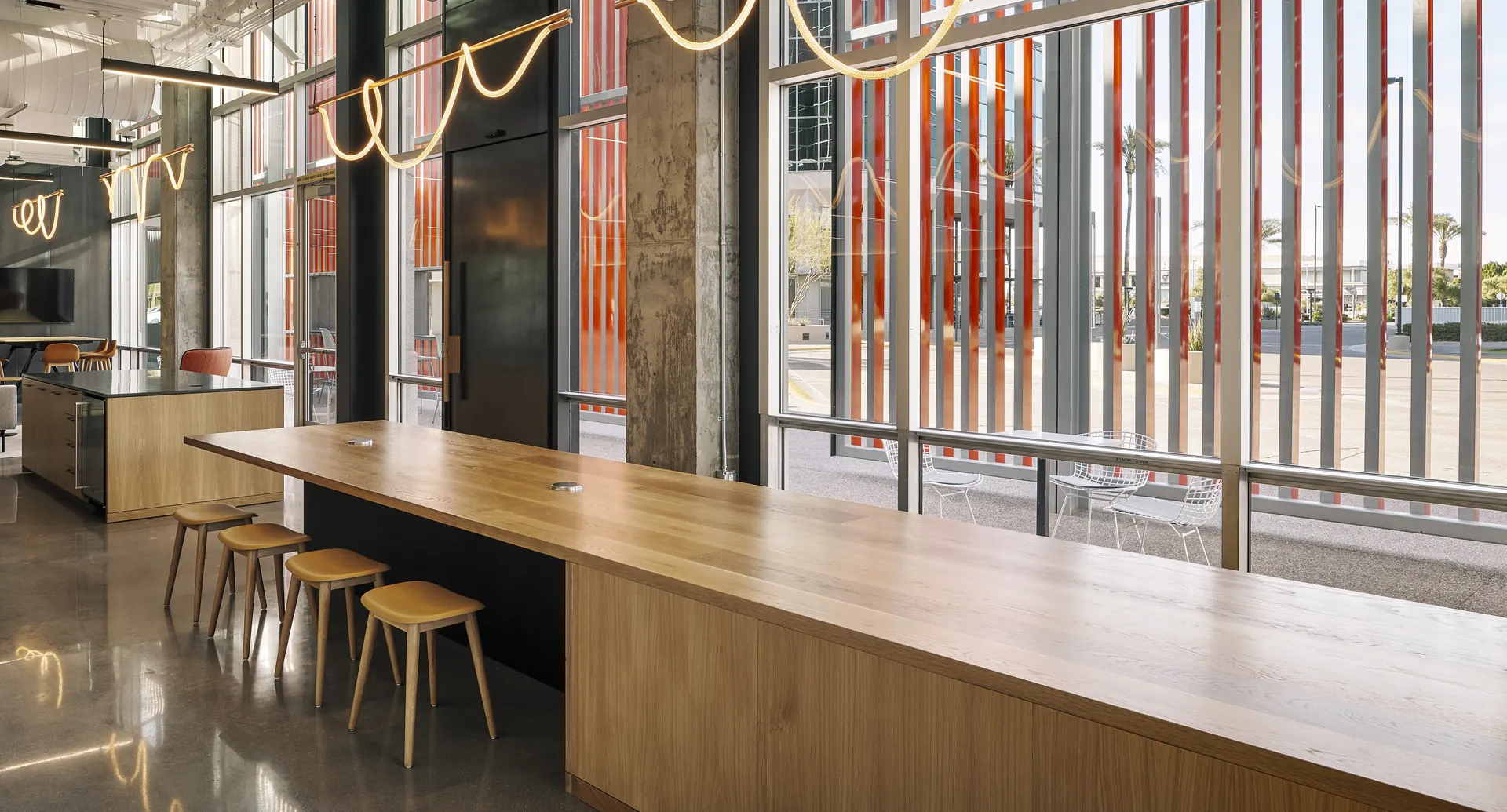 A long white oak communal counter and stools along a glass storefront in a commercial interior